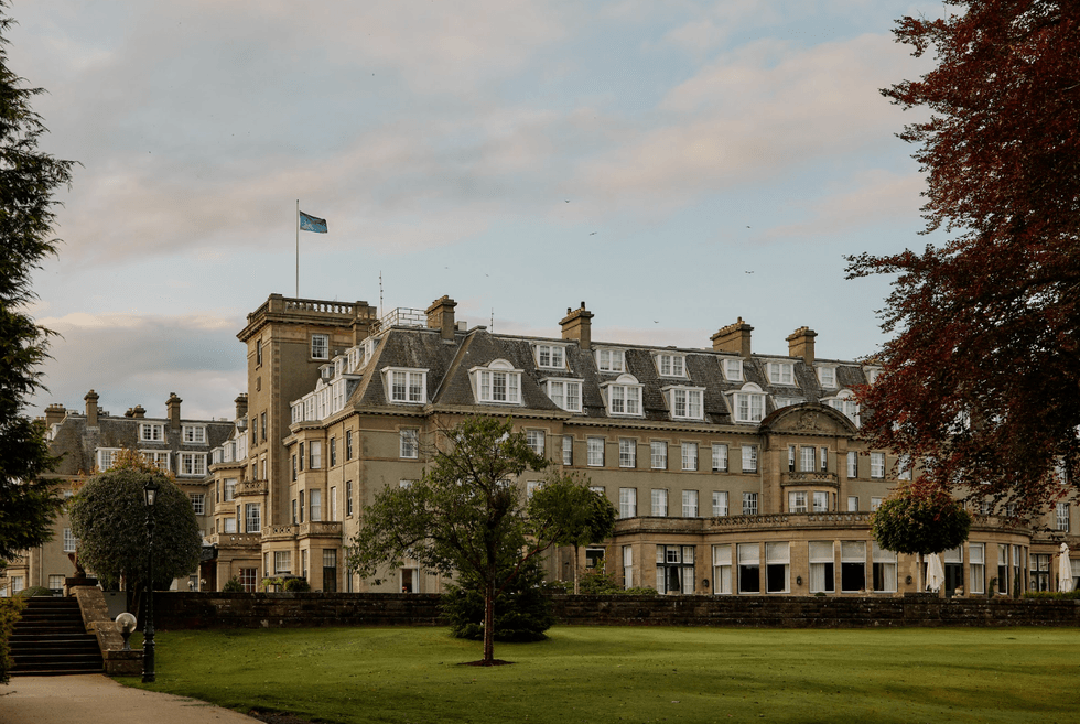 Grand historic hotel with large windows, surrounded by trees and a lush lawn.