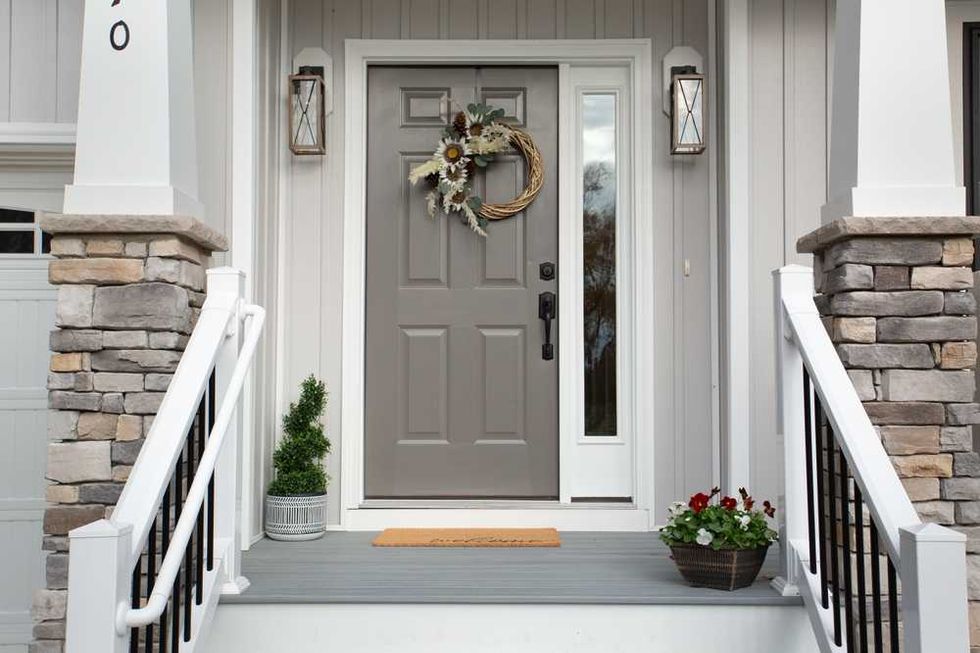 Gray front door with wreath, stone pillars, and flower pots on a staircase landing.