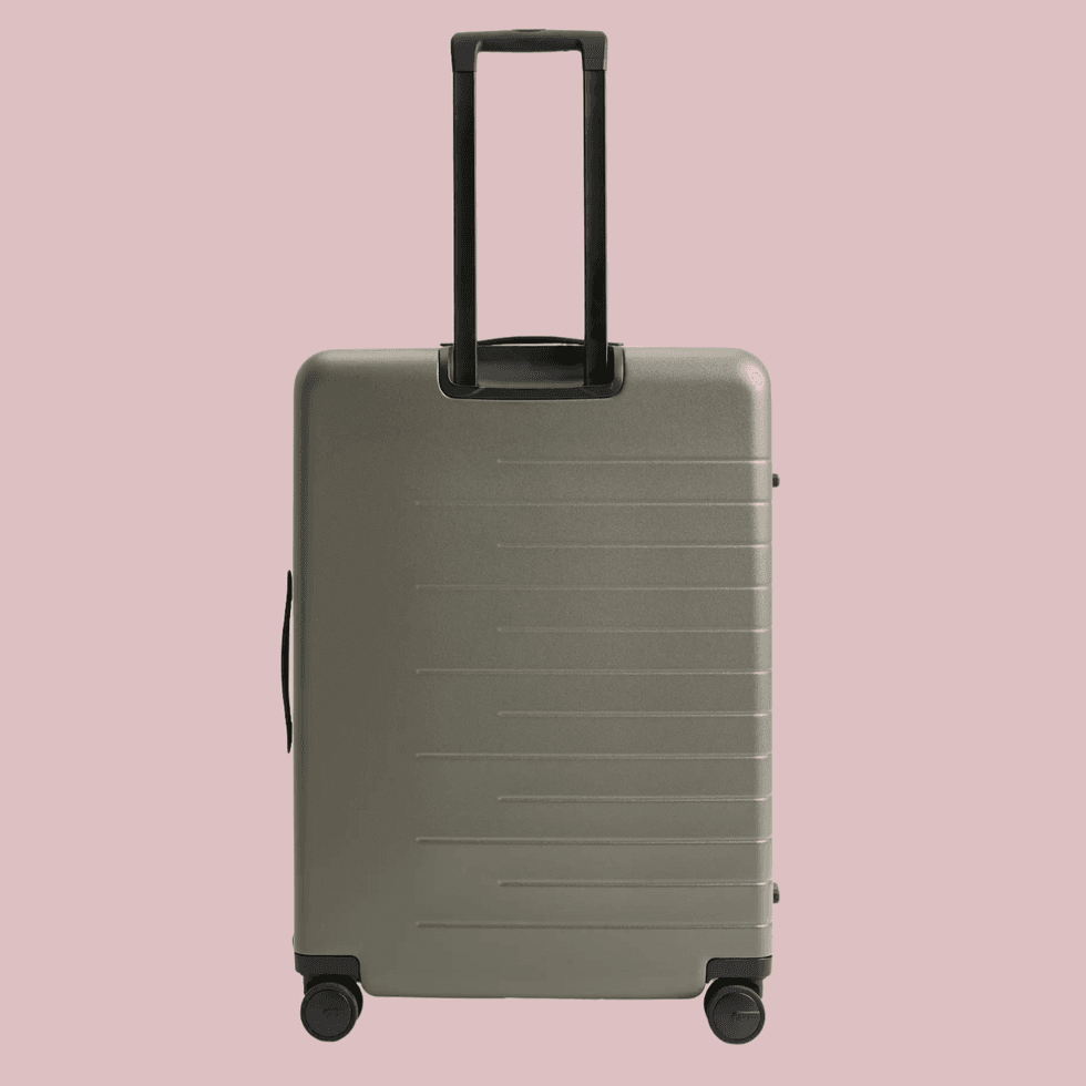 Gray hard-shell suitcase with black handle and wheels on a pink background.