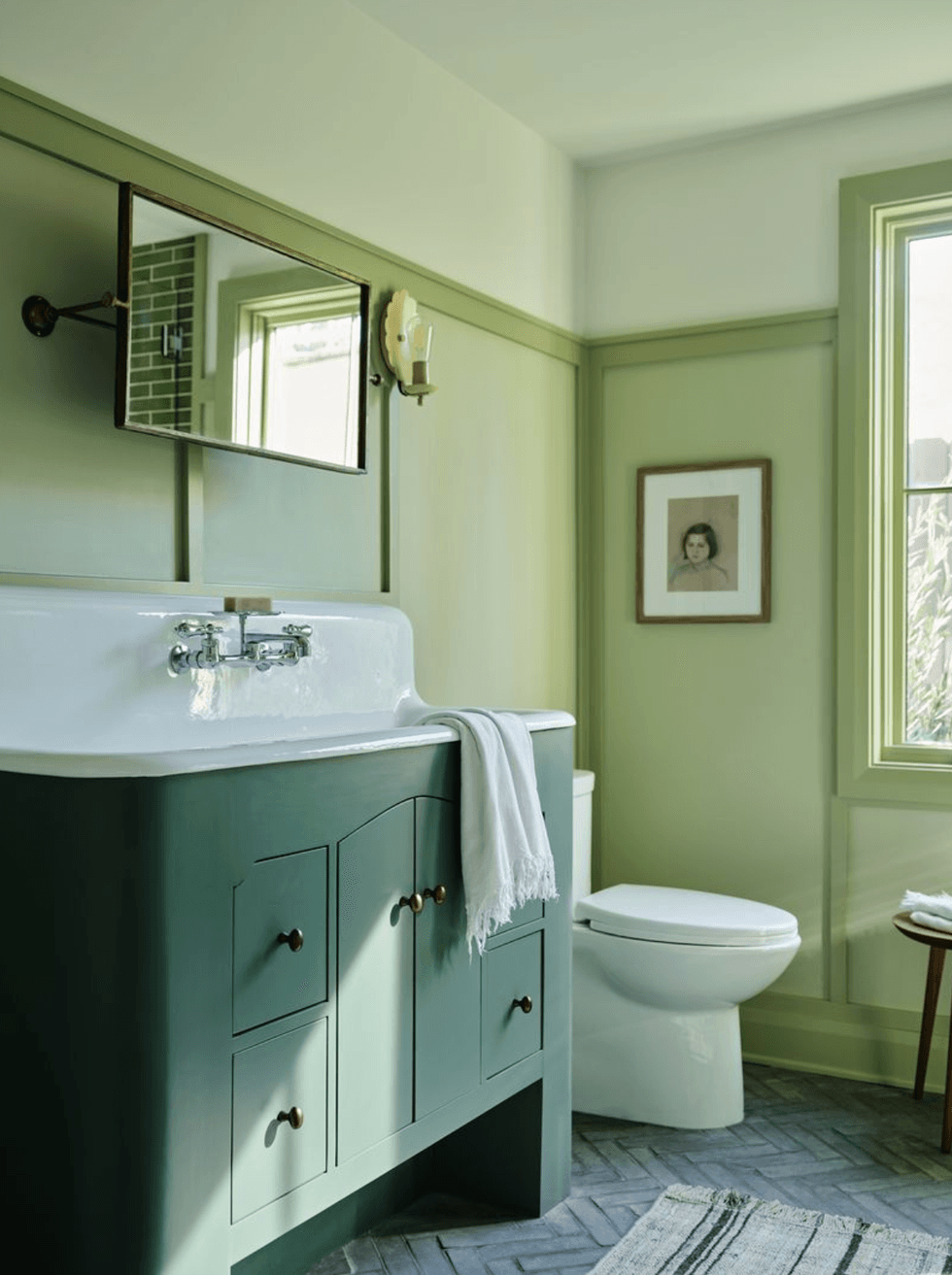 Green bathroom with vintage sink, wall mirror, and framed artwork on beige walls.