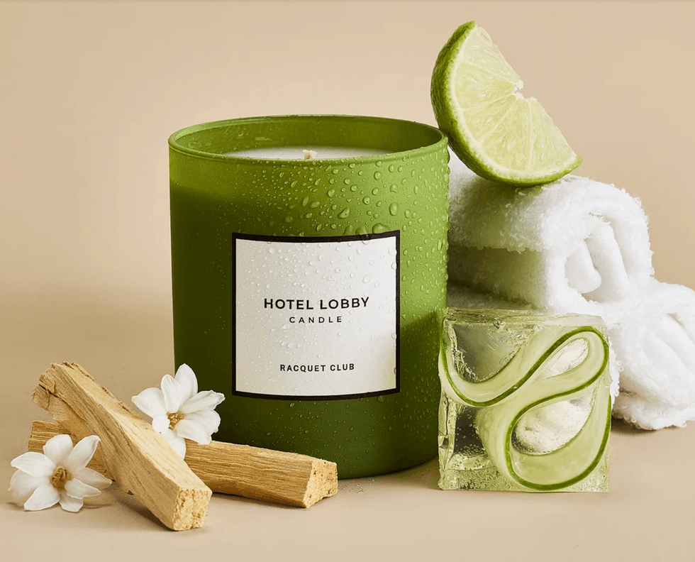 Green candle, lime slice, white flowers, wood sticks, and towels on a beige background.