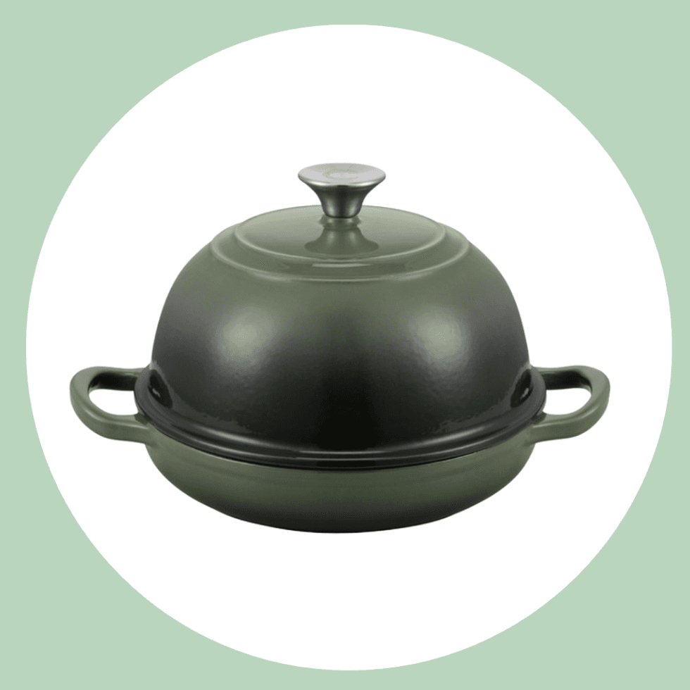 Green cast iron bread cloche with a domed lid and side handles on a white background.