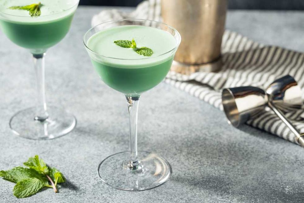 Green creme de menthe cocktails with mint garnish in coupe glasses on a grey surface.