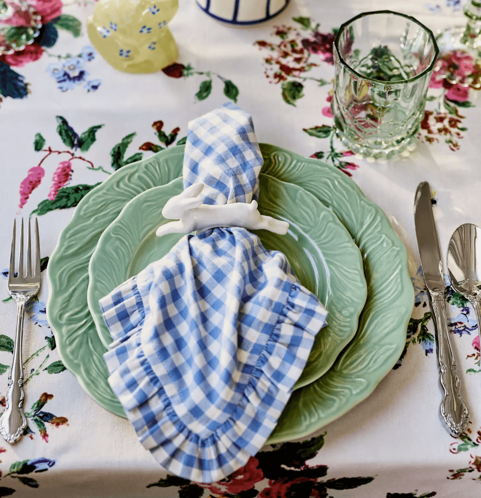 Green plates with blue gingham napkin on floral tablecloth setting.