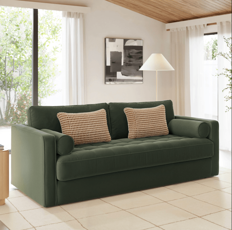 Green sofa with checkered pillows in a modern living room with large windows.
