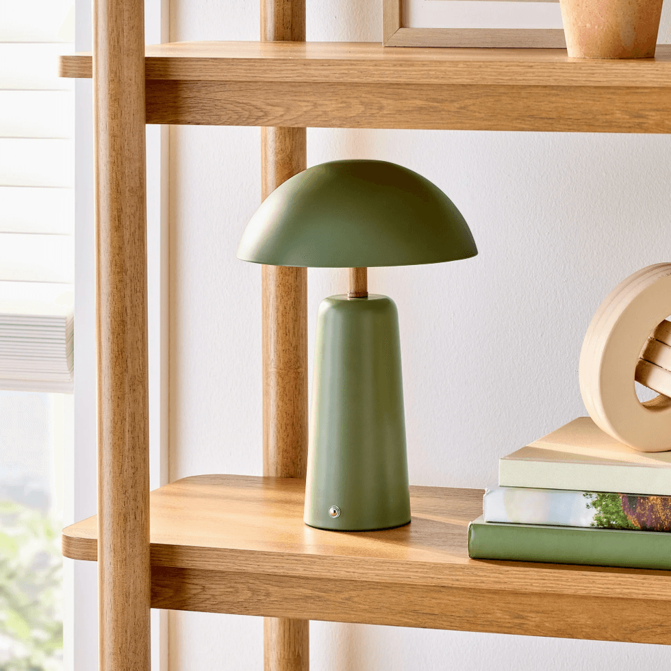 Green table lamp on wooden shelf with books and decorative items.