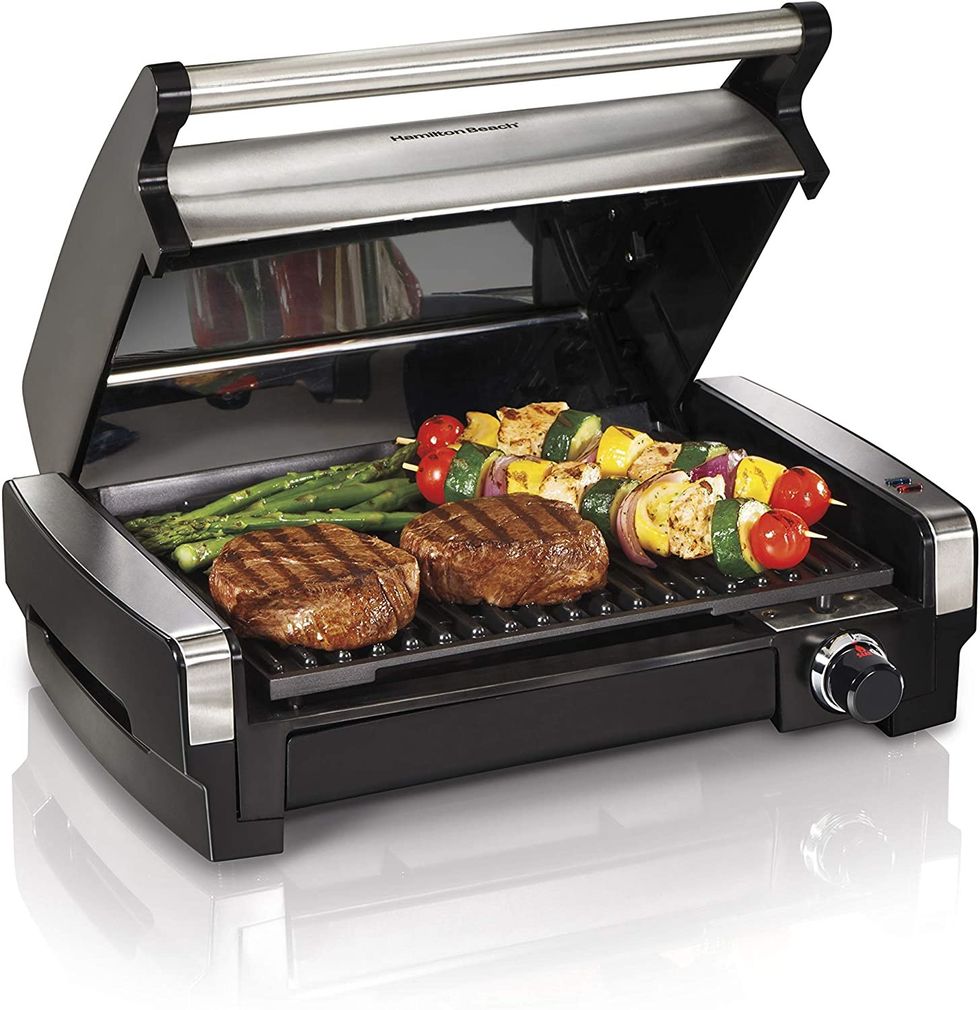 Grill with steaks, vegetable skewers, and asparagus on cooking surface.