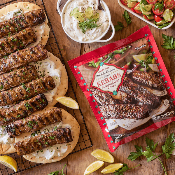 Grilled beef kebabs on flatbreads, with a salad, sauce, and lemon wedges.