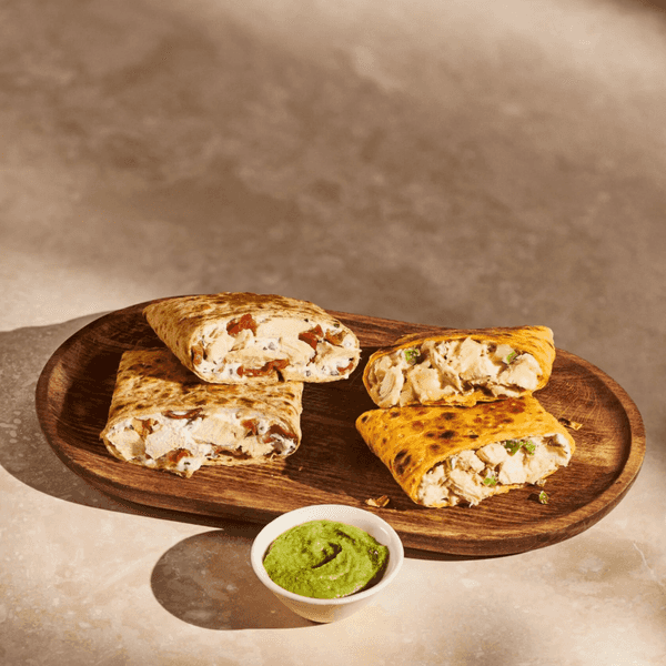 Grilled chicken wraps on a wooden plate with a bowl of green sauce.