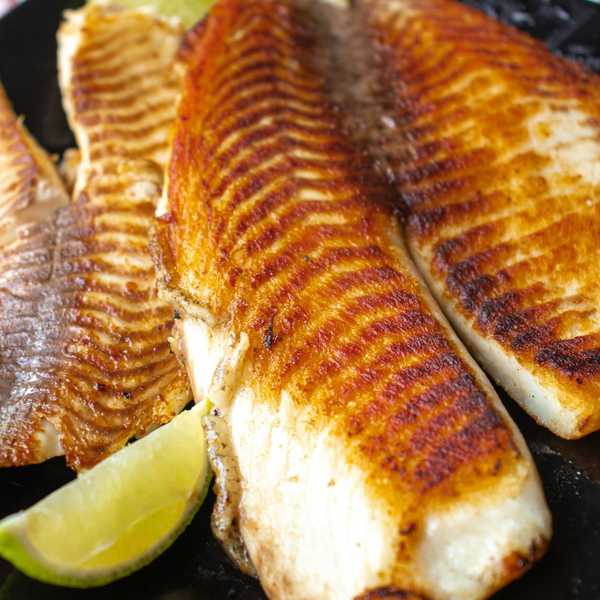 Grilled fish fillets with crispy skin, served with lime wedges.