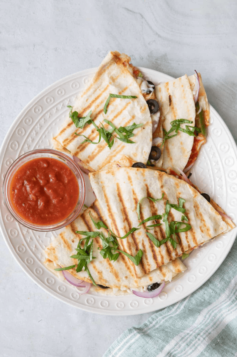 Grilled quesadillas with herbs and salsa on a white plate.