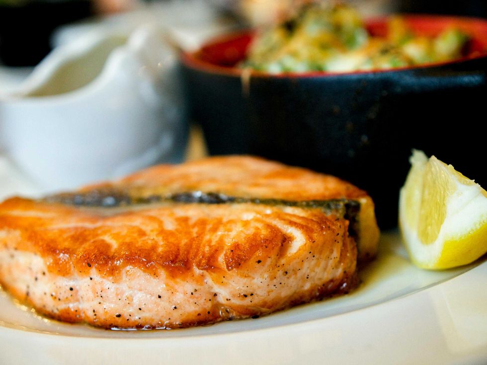 Grilled salmon steak on a plate with a lemon wedge and sauce on the side.