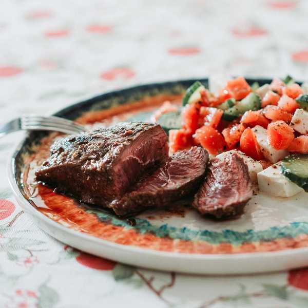 Grilled steak with a fresh cucumber and tomato salad on a patterned plate.