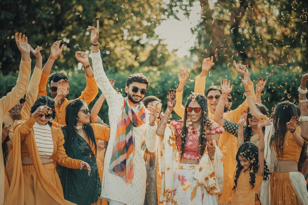 Group celebrating outdoors with colorful outfits and raised hands, surrounded by falling petals.