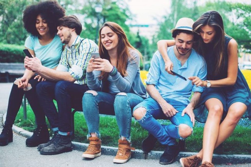 Group of mixed race people looking at mobile phones outdoors in the park