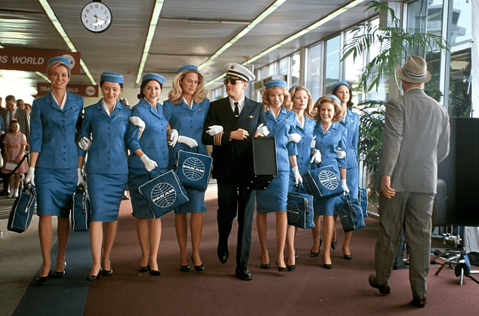 Group of Pan Am flight attendants and pilot walking in an airport.
