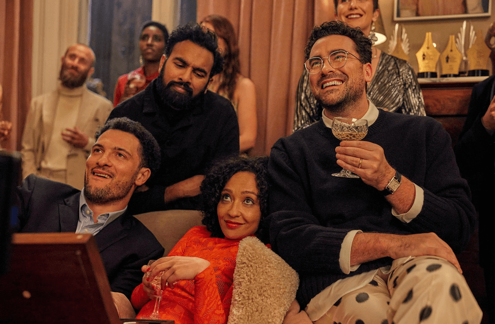 Group of people at a party, smiling and holding drinks, seated on a couch.