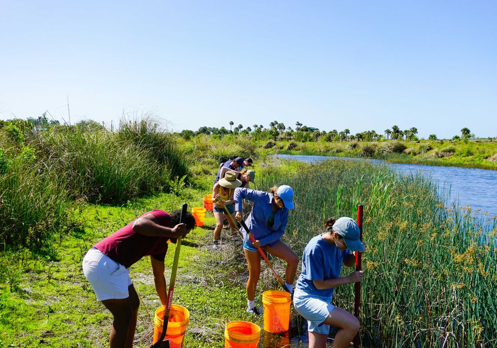 Group of people working with tools near a grassy waterway.