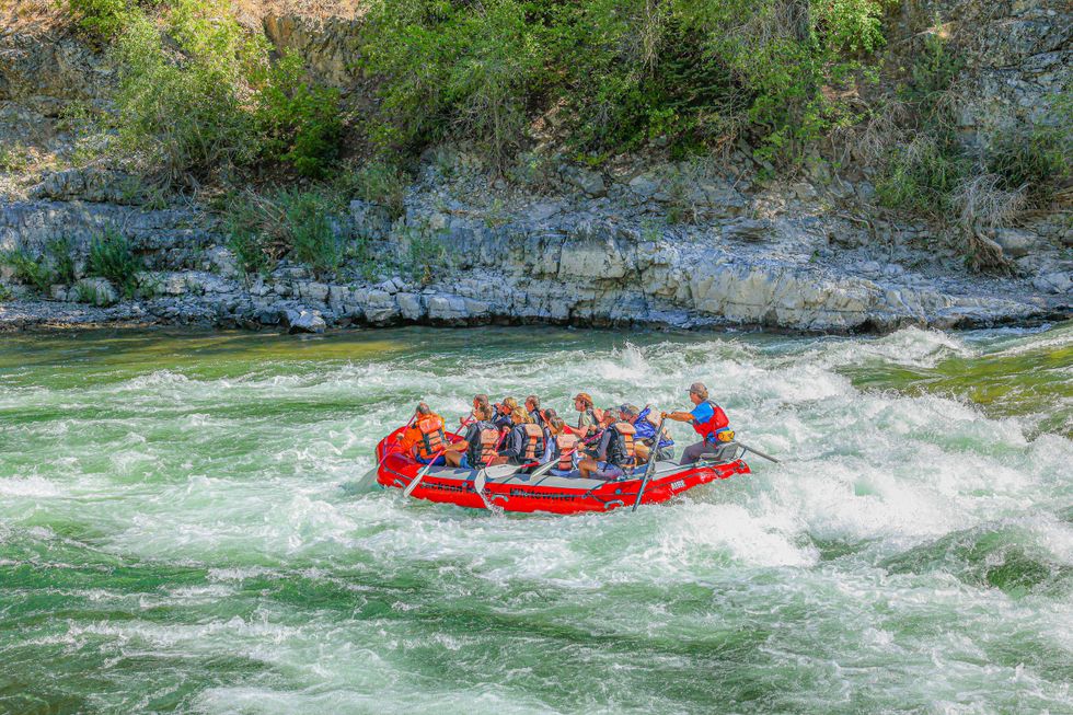 Group rafting on a rapid river, surrounded by rocky, forested cliffs.