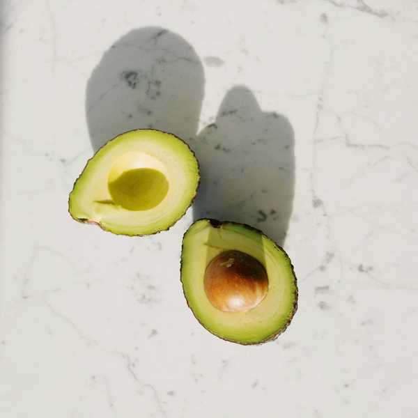Halved avocado on marble surface casting shadows.