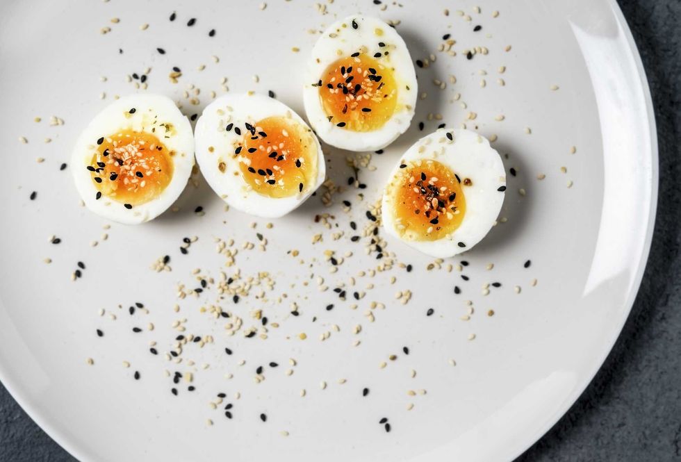 Halved soft-boiled eggs with sesame seeds on a white plate.