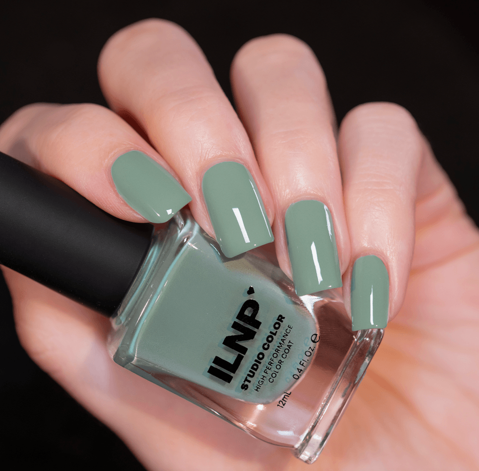 Hand holding a bottle of green ILNP nail polish, nails painted in matching color.