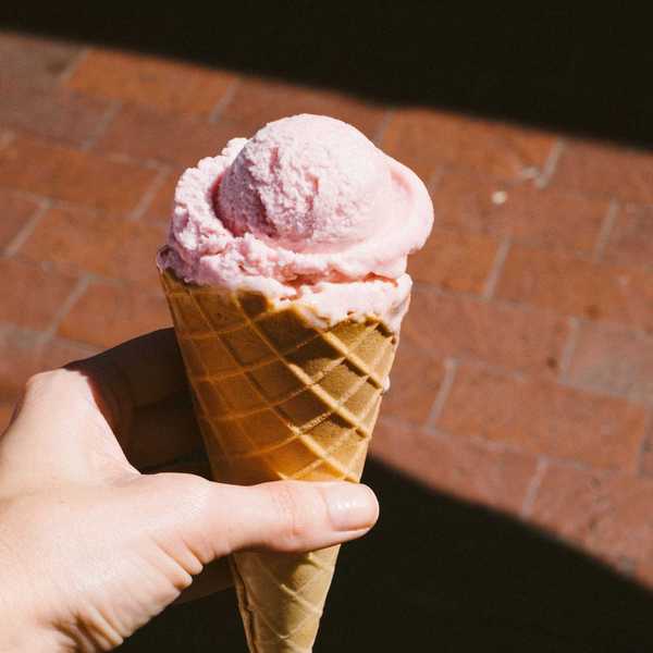 Hand holding a pink ice cream cone on a sunny day.