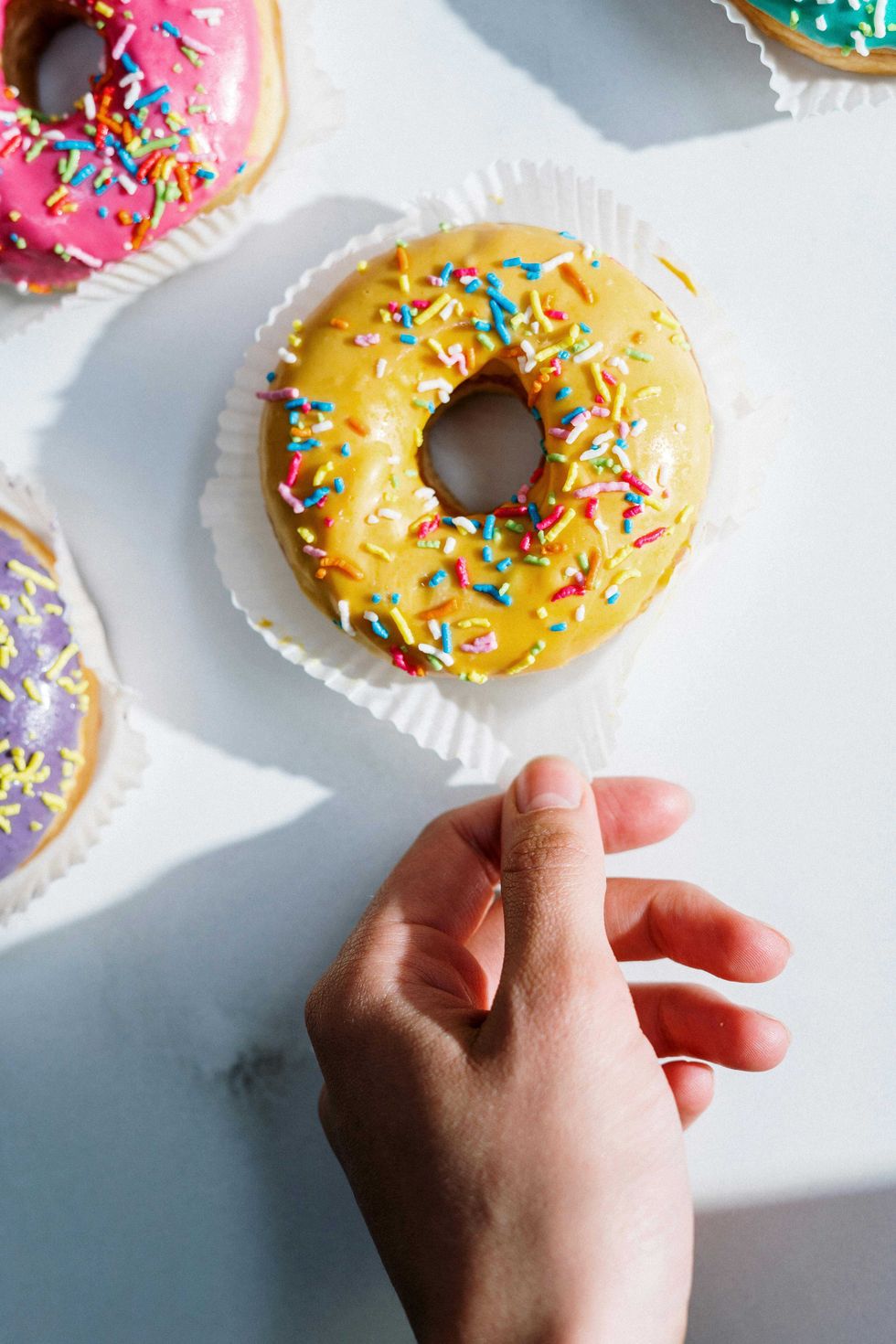 Hand holding a yellow donut with colorful sprinkles.