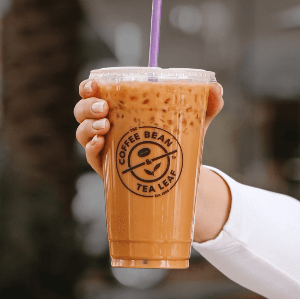 Hand holding iced coffee with a purple straw, Coffee Bean & Tea Leaf logo visible.
