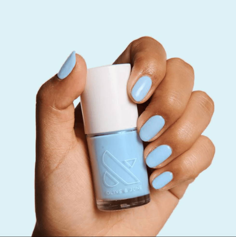 Hand holding light blue nail polish, nails painted light blue.