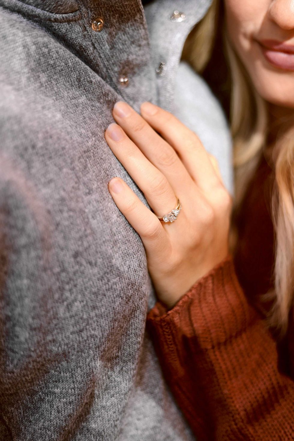 Hand on gray coat with diamond ring, close-up shot.