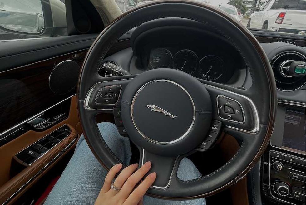 Hand on Jaguar steering wheel, dashboard view, inside a parked car.
