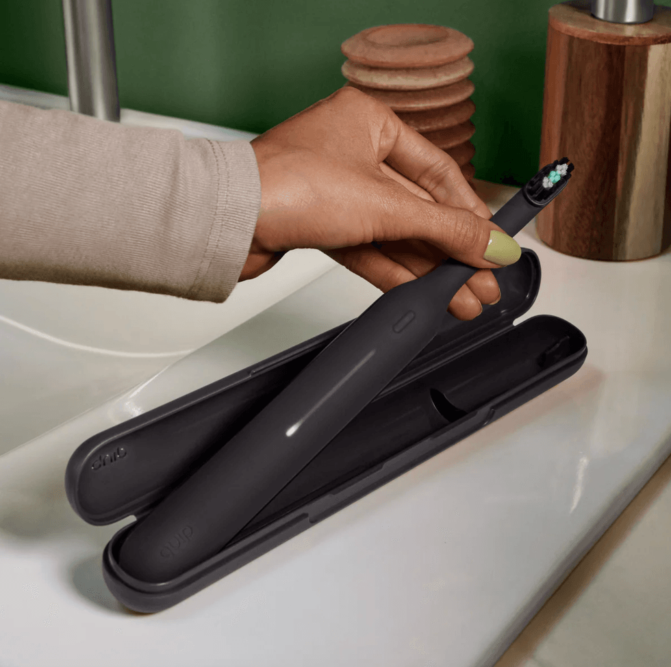 Hand placing a black electric toothbrush into a matching case on a bathroom sink.