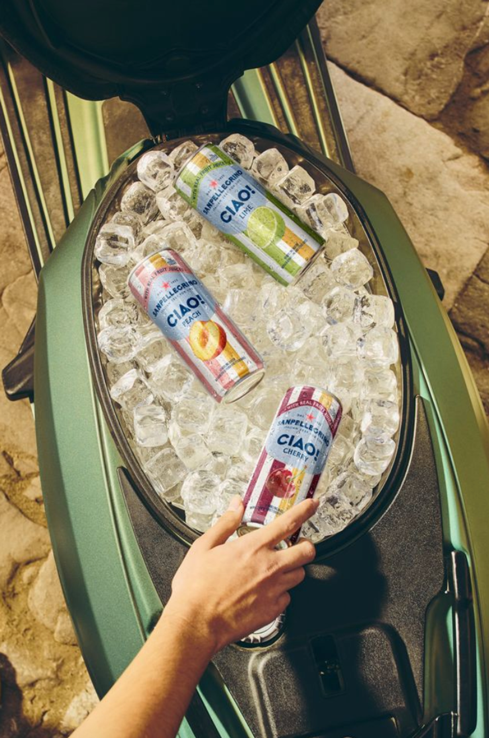 Hand reaching for a chilled can in a cooler with ice, featuring Sanpellegrino drinks.