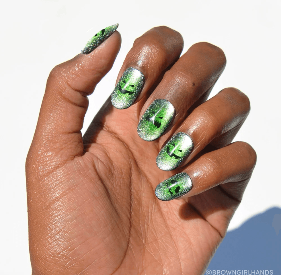 Hand with green Halloween-themed glitter nails featuring black jack-o'-lantern faces.