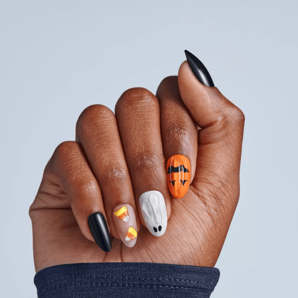 Hand with Halloween-themed nails: black, candy corn, ghost, pumpkin designs.