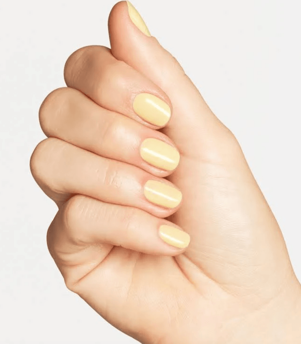 Hand with light yellow polished nails on a white background.