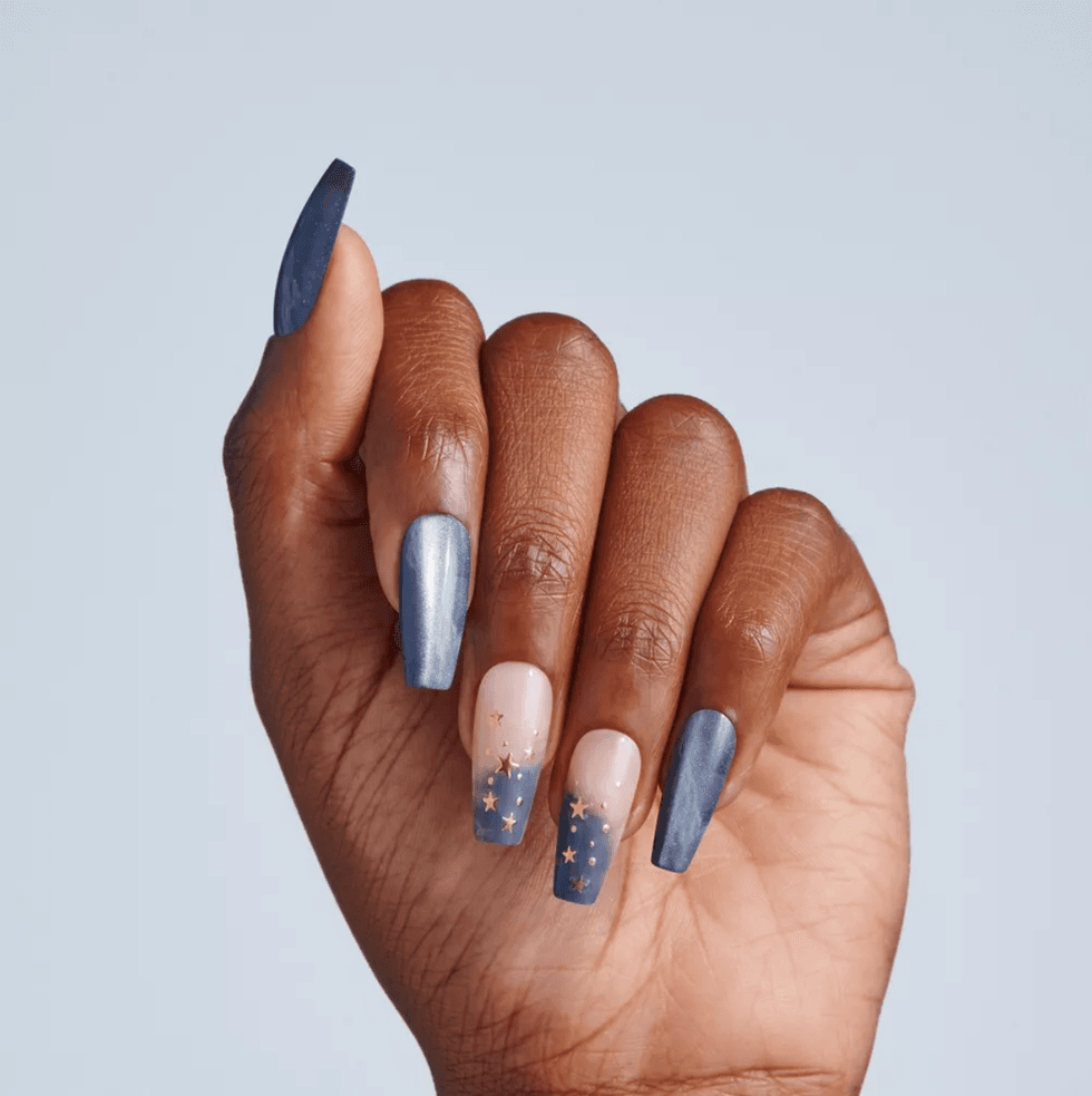 Hand with long blue nails, star designs on two nails, against a light background.