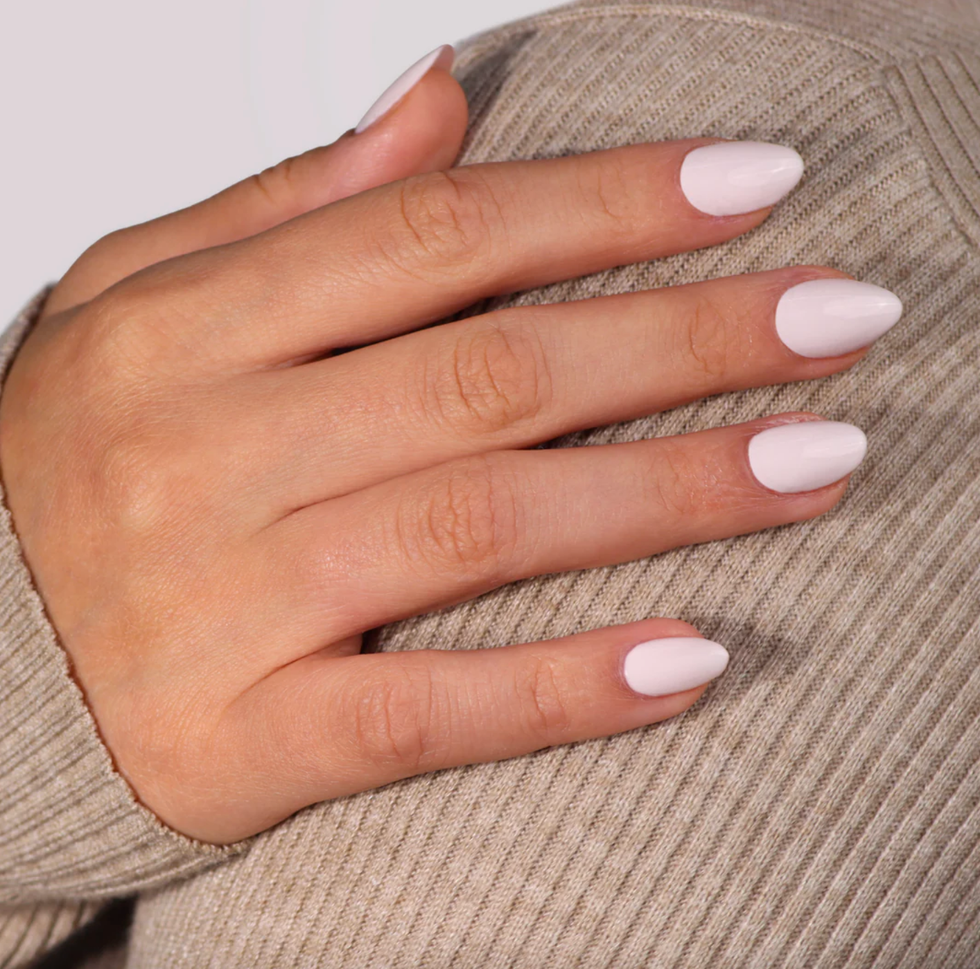 Hand with long, pastel pink nails on a beige textured fabric.