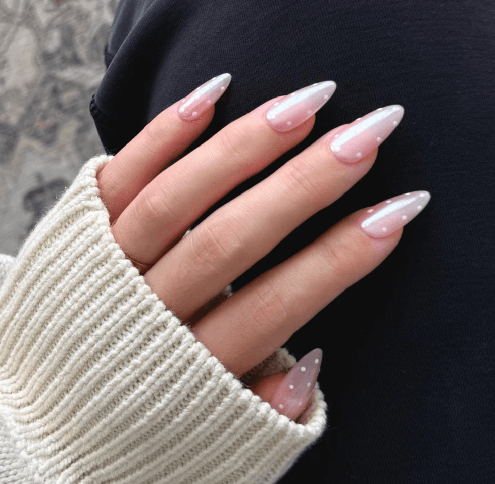 Hand with pink and white polka dot nails, wearing a cream sweater.