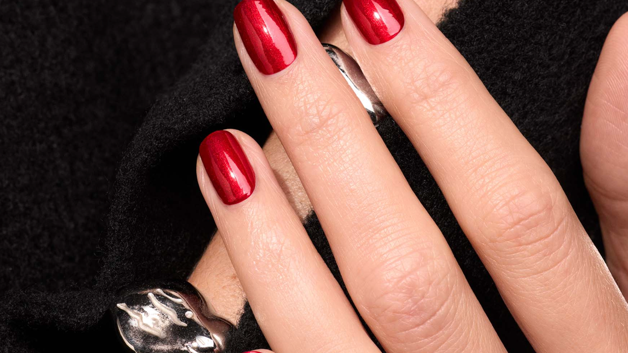 Hand with red nails and silver rings on a black fabric background.