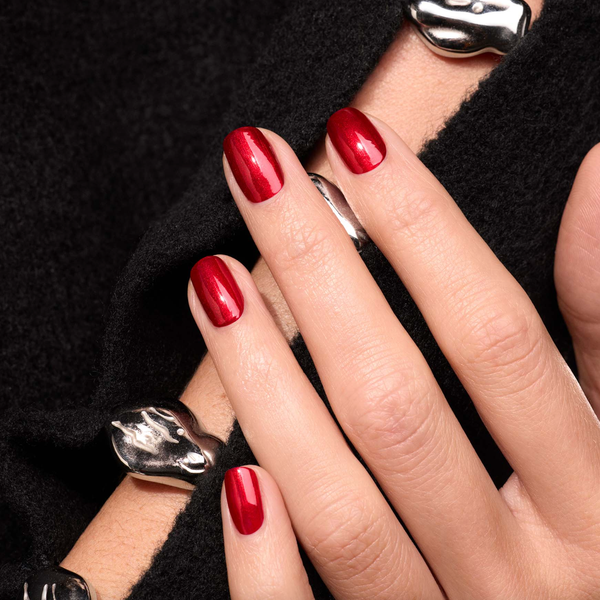 Hand with red nails and silver rings on a black fabric background.