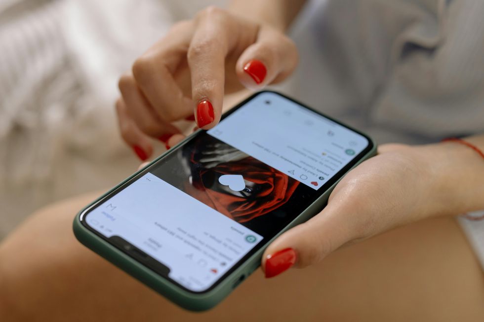 Hand with red nails tapping a smartphone screen, displaying a social media post.