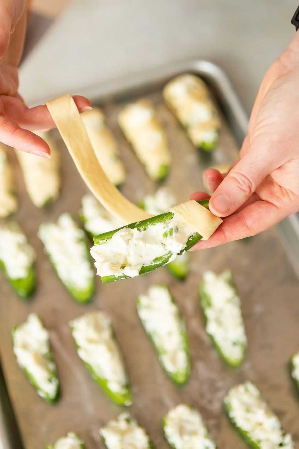 Hand wraps cheese-filled jalape\u00f1o with pastry on a baking tray.