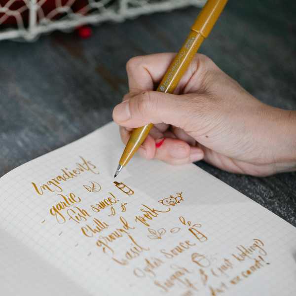 Hand writing ingredients list with a golden pen in a notebook.