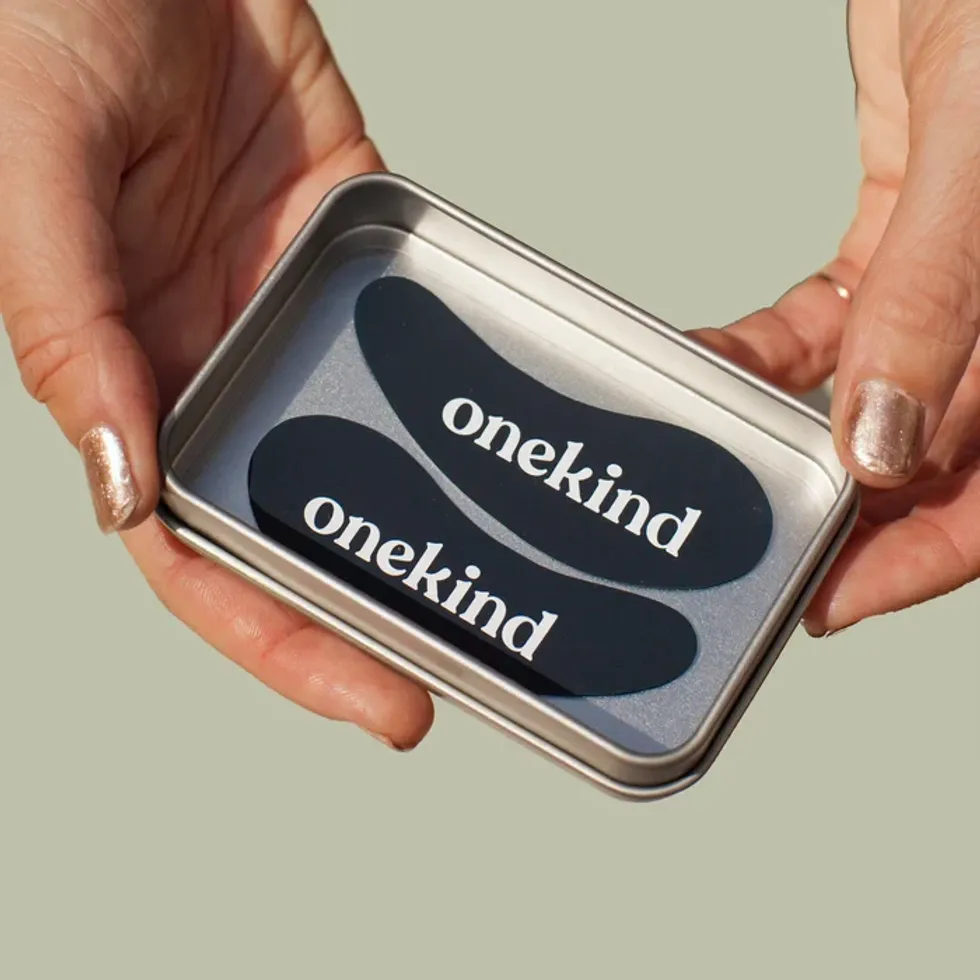 Hands are holding a container of Onekind under-eye masks.