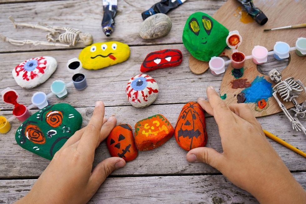 Hands arranging colorful, Halloween-themed painted stones on a wooden table.