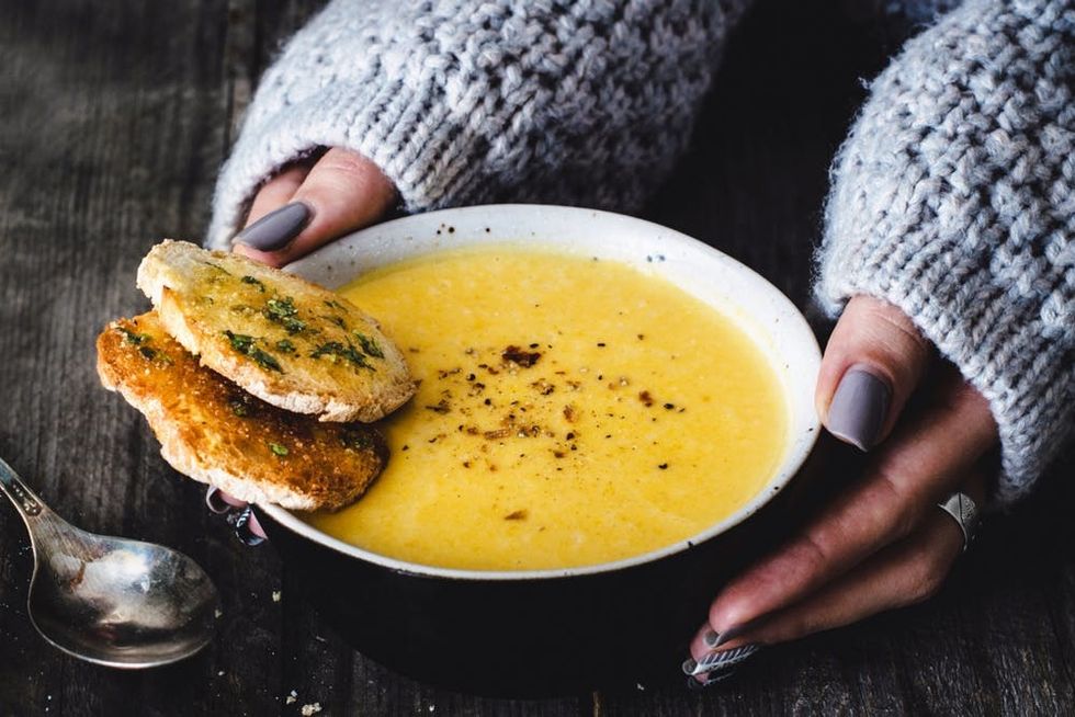 Hands hold a warm bowl of carrot pumpkin cream soup