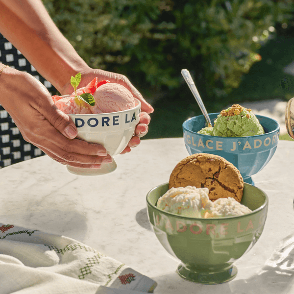 Hands holding a bowl of strawberry ice cream; other bowls with cookies on a table.
