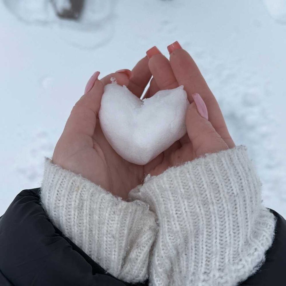 Hands holding a heart-shaped snowball on a snowy background.
